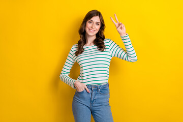 Photo of optimistic cheerful good mood smile youngster woman show v-sign put hand denim jeans friendly person isolated on yellow color background
