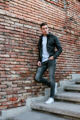 A fashion male model on staircase. Young attractive caucasian man wearing black leather jacket and...