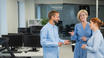 Fototapeta premium Colleagues communicate at work. Red-haired woman, blonde and bearded man in a denim shirt in the office.