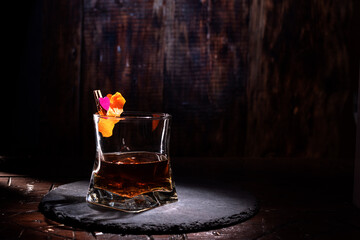 A glass of cognac and an orange peel. Whiskey in a dark bar. A beam of light on a glass with a...