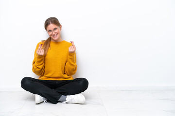 Young caucasian woman sitting on the floor isolated on white background making money gesture