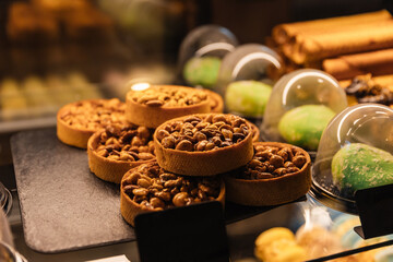 Tartlets with peanuts and caramel in the window of a coffee shop under the light. A sweet, nutty, delicious dessert. Baking with nuts