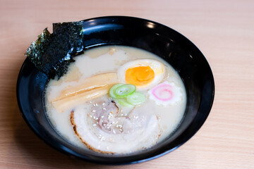 Tonkotsu ramen in a black cup topped with chashu pork, Naruto fish balls, soy-sauce pickled eggs, menma bamboo shoots and seaweed. Ramen is a distinctive Japanese style noodle soup.