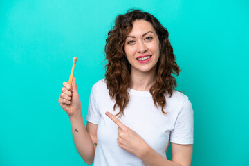 Young caucasian woman brushing teeth isolated on blue background and pointing it