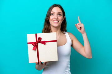 Young caucasian woman holding a gift isolated on blue background intending to realizes the solution while lifting a finger up