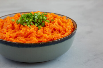 Homemade Creamy Mashed Sweet Potatoes with MIlk and Butter in a Bowl on a gray background, side view.
