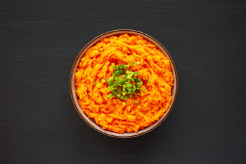 Homemade Creamy Mashed Sweet Potatoes with MIlk and Butter in a Bowl on a black background, top view.
