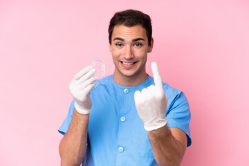 Dentist caucasian man holding invisible braces isolated on pink background doing coming gesture