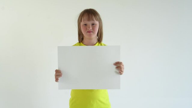A teenage girl with blond hair in a yellow T-shirt holds a sheet of A3 paper and smiles. mock up and space for text, Down syndrome awareness concept. International Down Syndrome Day.