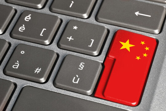 Button painted with the Chinese flag on grey laptop keyboard. Close-up view of flag of China on keyboard.
