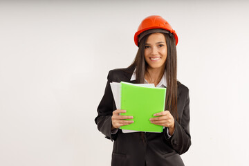 Portrait of happy young woman-architect-designer in business suit and orange helmet with documents in her hands on isolated white. Attractive brunette girl is working on construction project.