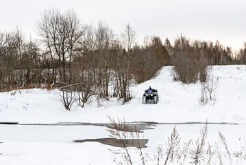A man driving his ATV across the river in the wilderness at winter.
