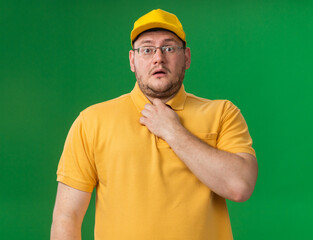 anxious overweight young deliveryman in optical glasses holding collar looking at camera isolated on green background with copy space