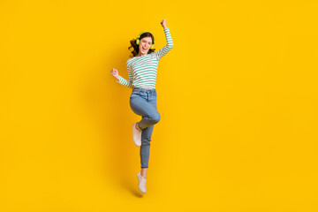Fototapeta na wymiar Full size photo of ecstatic woman dressed striped shirt jeans shoes clenching fists jumping high isolated on yellow color background