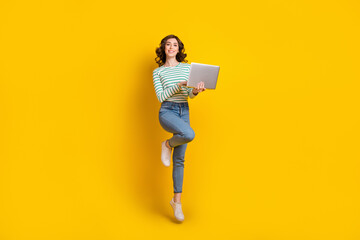 Full size photo of adorable cute nice cheerful woman dressed striped shirt jeans shoes hold laptop isolated on yellow color background