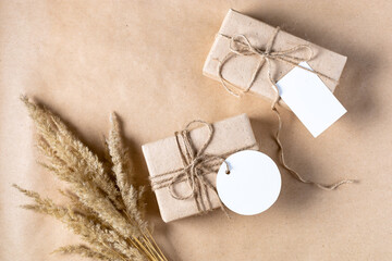empty white gift tag mock up on craft paper box with dried spikelets decoration on natural beige background.