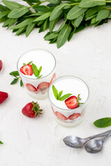 White yogurt with fresh strawberries granola and mint in two glasses on a white background.