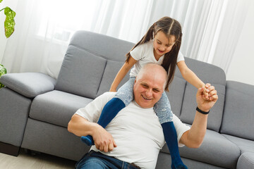 Cute little girl spending time with positive active grandpa in living room
