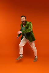 Fototapeta na wymiar Cheerful bearded man in green jacket jumping on red background.