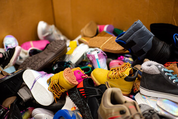 Mixed wide variety of brand new shoes tied in rubber band in large carton box at donation center in...