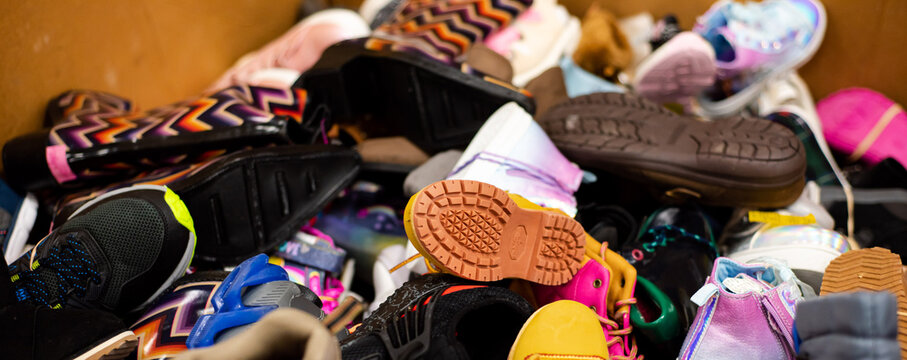 Panorama view mixed wide variety of brand-new shoes tied in rubber band in large carton box at donation center in Dallas, Texas, USA