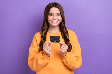 Photo of positive pretty lady wear orange sweatshirt holding credit card isolated violet color background