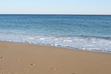 Fototapeta na wymiar Calm ocean side with wet sand under clear blue sky in Algarve, Portugal