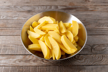 Chopped raw potato in metal bowl ready for cooking on wooden table, french fries.