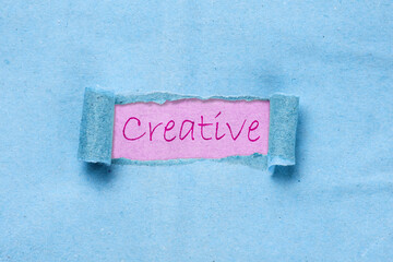 Creative word under torn blue paper.