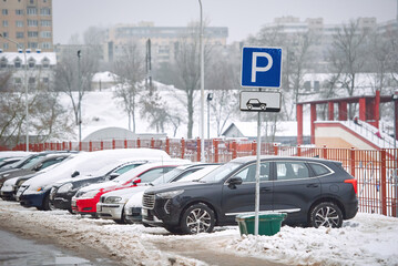 Cars parked on parking lot in cold winter season. Parking lot sign, cars parked on snowy parking in residential area. Parking problems not enough free space.