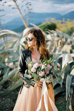 Bride in sunglasses with a bouquet of flowers stands near the agave bush