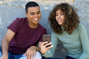 Hispanic male and female young adult couple watching movie online at mobile phone