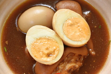boiled half cut egg with fat pork leg in herb brown soup on bowl 
