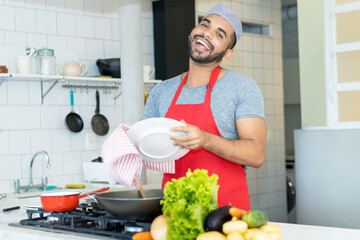 Handsome hispanic kitchen assistant cleaning plates at work