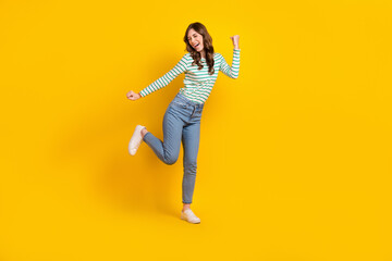 Full size photo of good mood crazy woman curly hairstyle striped shirt clenching fists having fun isolated on yellow color background