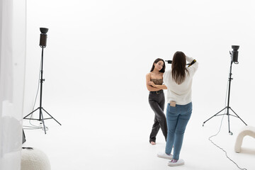 Photographer shoots woman posing in studio against white background.