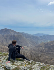 A man sits on a mountain and looks into the distance nature hiking on foot travel