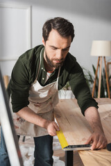 Bearded carpenter using square tool on wooden board in workshop.