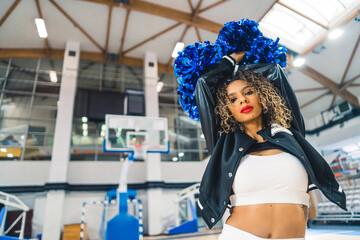 confident curly-haired cheerleader holding pom-poms up n her head, medium shot. High quality photo