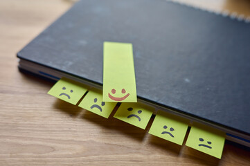 Lachende und traurige Gesichter auf post it Zettel in einem Notizbuch auf einem Schreibtisch aus Holz. 