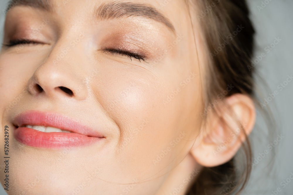 Wall mural close up view of pleased young woman with natural makeup closing eyes isolated on grey.