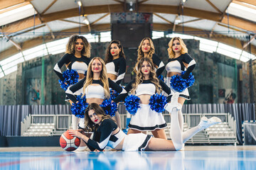Obraz premium team of beautiful cheerleaders in black-white uniforms posing for the camera together, indoors. High quality photo