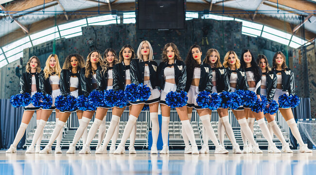 full shot of Caucasian confident cheerleaders standing in a raw ad posing in the arena. High quality photo
