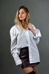 Young woman in a studio, in a shirt and a mini skirt, poses