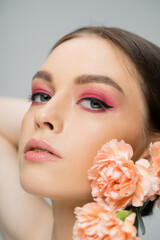 peach carnations near sensual woman with pink makeup looking at camera isolated on grey.