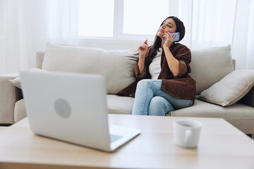 Obraz premium Woman blogger with phone lying at home and talking on the phone on sofa with laptop and working freelancer online, smiling with teeth