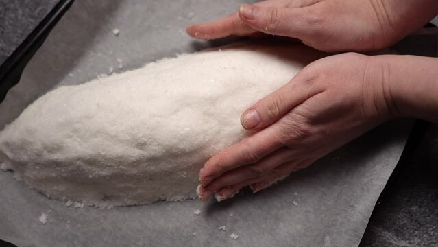 The chef forms a salt cocoon with raw fish inside before baking. The process of cooking fish in a salt shell flamb&eacute; in the oven. Close up shot from above