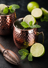 Moscow mule cocktail in a copper mug with lime and mint and wooden squeezer on dark kitchen table background.