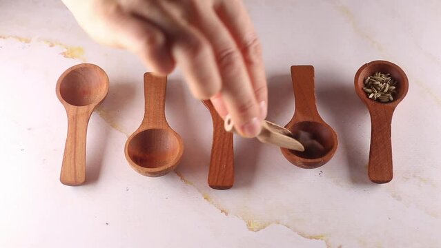 Different spices in wooden spoons process of putting by woman hand