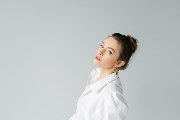 portrait of young model in white oversize shirt looking at camera isolated on grey.
